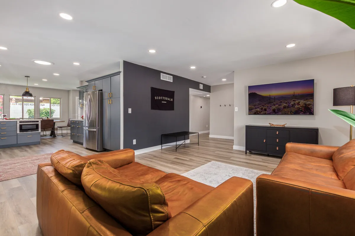 Showcasing a living space that flows into a modern kitchen, this image includes brown leather sofas, contemporary wall art, and a glimpse of an open-concept layout. The arrangement is ideal for social gatherings, movie nights, and relaxed entertaining.