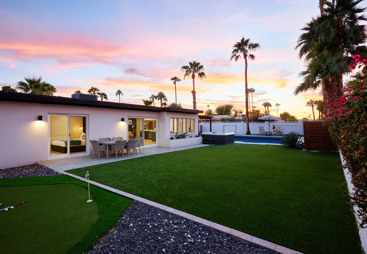 This exterior image features a lush green lawn with a mini golf area, a sparkling swimming pool, and a patio seating area, all set against a beautiful sunset backdrop. The open, inviting space is perfect for families to play, relax, and dine outdoors together.