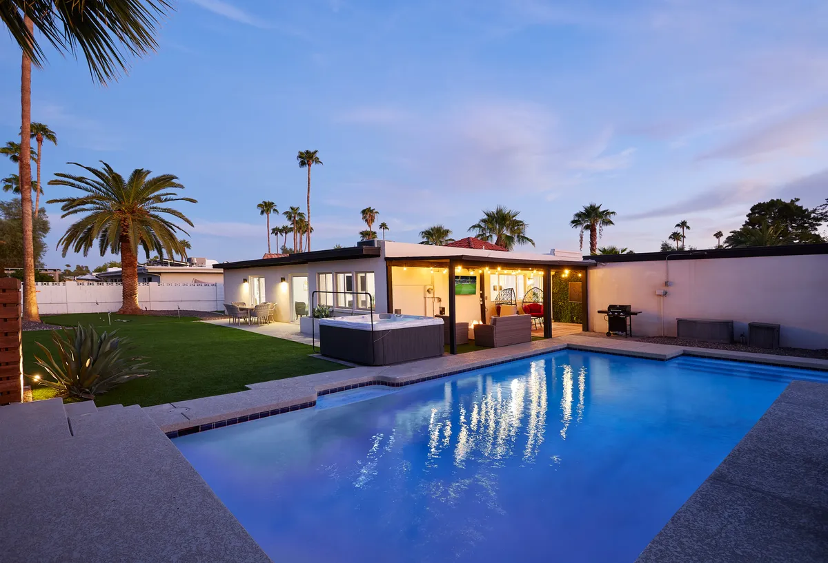A luxurious backyard with a sparkling swimming pool, a soothing hot tub, tall palm trees, and comfortable outdoor seating. The space is designed for relaxation after a day on the links, with both sun and shade areas for unwinding.