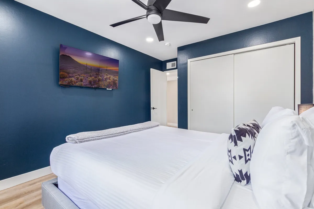 A cozy bedroom with crisp white linens on the bed, a wall-mounted television, and a dramatic dark blue accent wall. Nightstands flank the bed, and soft lighting creates an inviting atmosphere perfect for lounging or unwinding with a favorite show after a day of adventure.