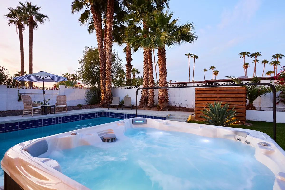 An inviting outdoor resort scene featuring a hot tub and swimming pool surrounded by palm trees and a tranquil outdoor seating area, photographed at sunset. The setting is serene and luxurious, suggesting relaxation and indulgence after a day spent exploring the city.
