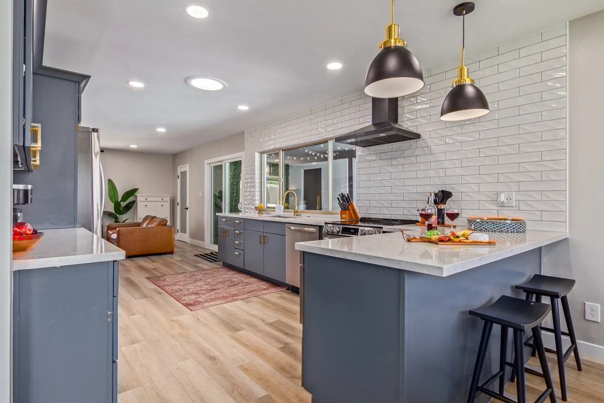 A warm, welcoming kitchen scene with a prominent kitchen island, stylish pendant lights, large window, and gleaming stainless steel appliances. The space feels ready for both culinary endeavors and social gatherings with family and friends.