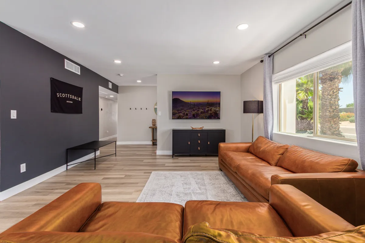 This image captures a welcoming living room with a leather sofa, elegant artwork on the wall, a statement light fixture, and a window that frames attractive outdoor views. The layout suggests a space ideal for cozy conversations, relaxing with coffee, or enjoying the sunset through the window.
